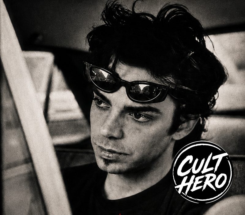 Will Keenan in black and white, sunglasses pushed up on his head, behind the wheel of a car